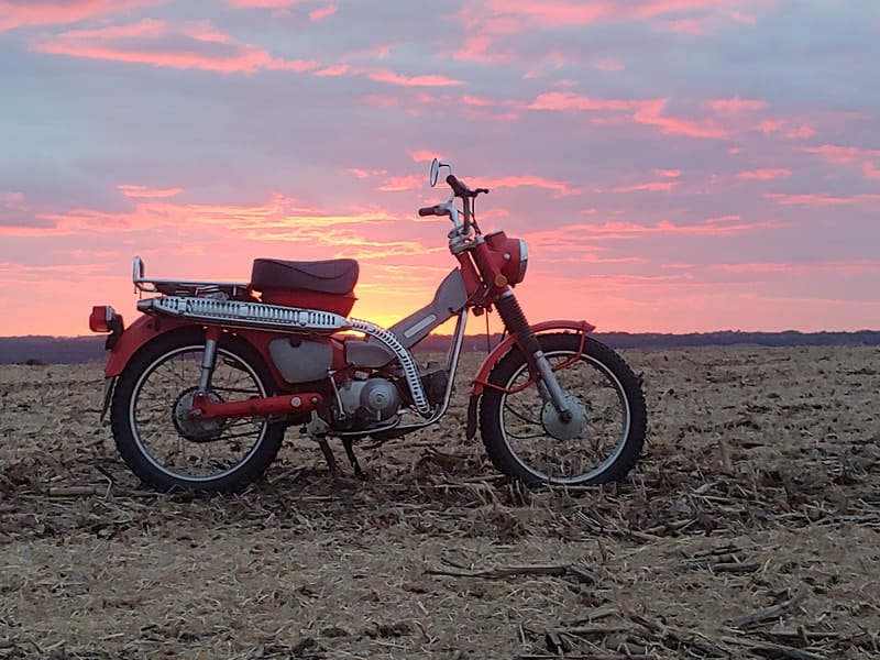 Vintage Honda Trail motorcycle in a harvested field at sunset
